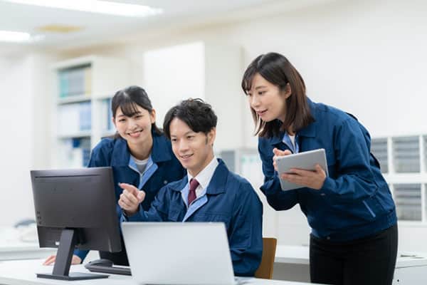 作業服を着た3人の男女が一緒にPCを見る様子